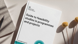 Front cover of a report titled “Guide to feasibility studies in programmes and projects” with the Government Project Delivery logo. The report is placed on a light surface next to a notebook, pencil and dried flowers.